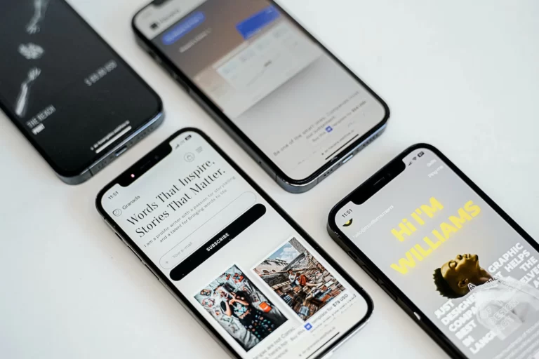 Four smart phones with different websites loaded have been placed diagonally on a white surface.
