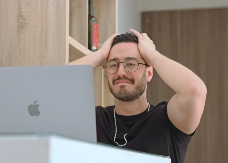 A man in front of a laptop looking frustrated.