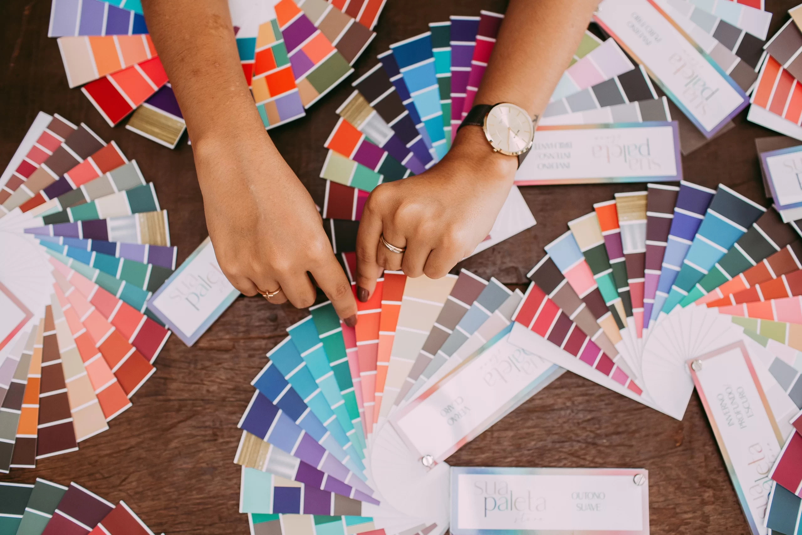 A person’s hands manipulating a fanned out color chart with more color charts in the background. Photo: Helena Lopes